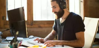 En mann sitter foran en PC skjerm med headset. Foto