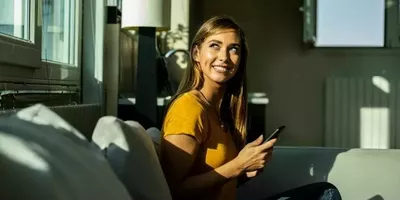 En dame sitter i en sofa og smiler. Foto