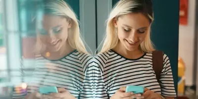 En dame lener seg til en glassvegg og ser på telefonen sin. Foto