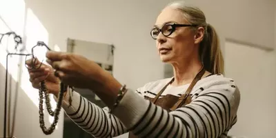 En dame henger opp smykker på et stativ. Foto