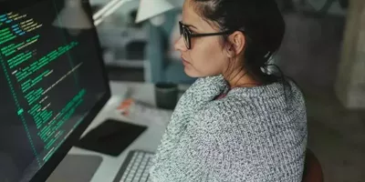 En dame sitter foran en skjerm med kodespråk. Foto